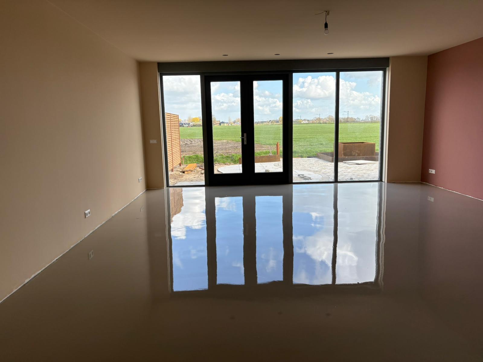 Glanzende gietvloer in een lege woonkamer met uitzicht op een weiland