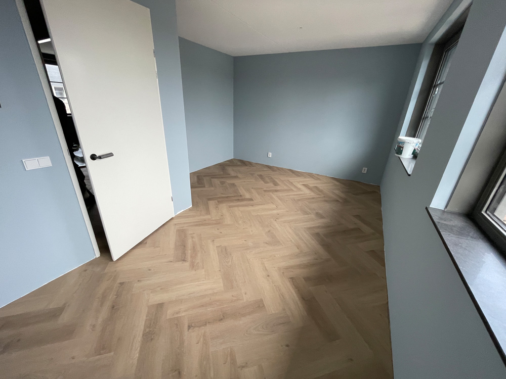 Slaapkamer met blauwe wanden en een eiken visgraatvloer
