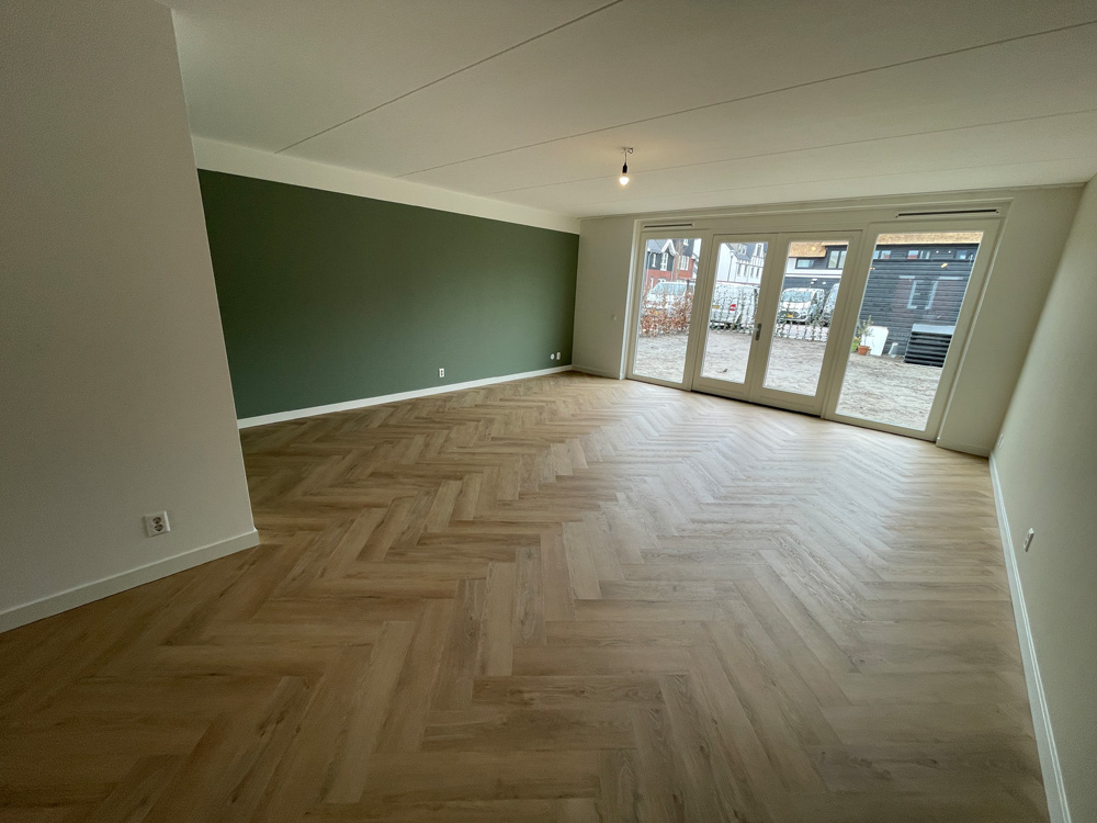 Woonkamer met groene wand en een eiken PVC visgraatvloer